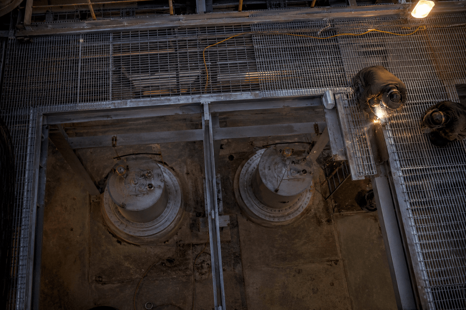 Steel gantry and tank-support framework mid-installation at night, weld arc visible